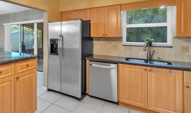 kitchen with light tile patterned floors, a sink, dark stone counters, appliances with stainless steel finishes, and decorative backsplash