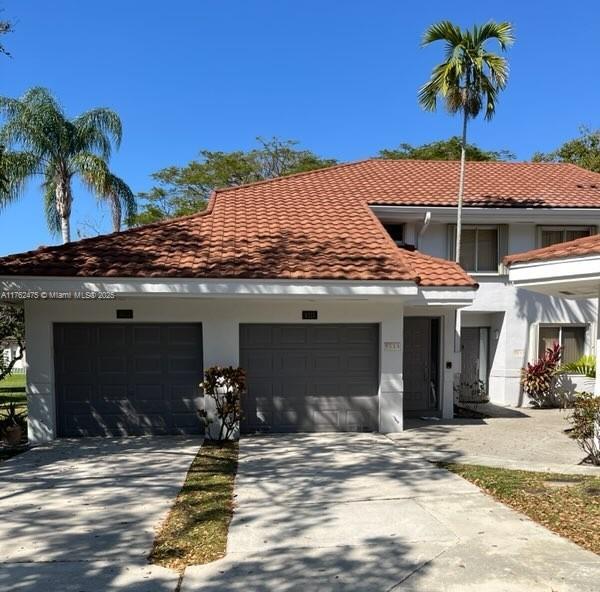 mediterranean / spanish house featuring stucco siding, a tiled roof, an attached garage, and driveway