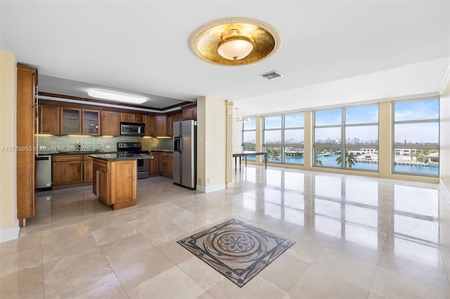 kitchen with visible vents, backsplash, a kitchen island, glass insert cabinets, and stainless steel appliances