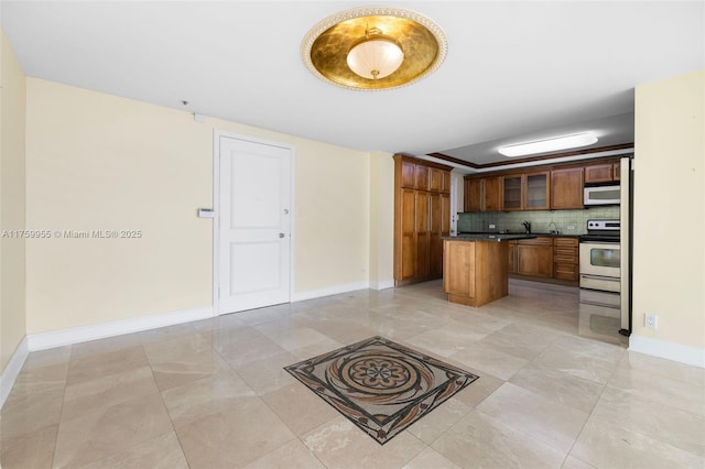 kitchen with white microwave, dark countertops, stainless steel electric range oven, decorative backsplash, and brown cabinetry