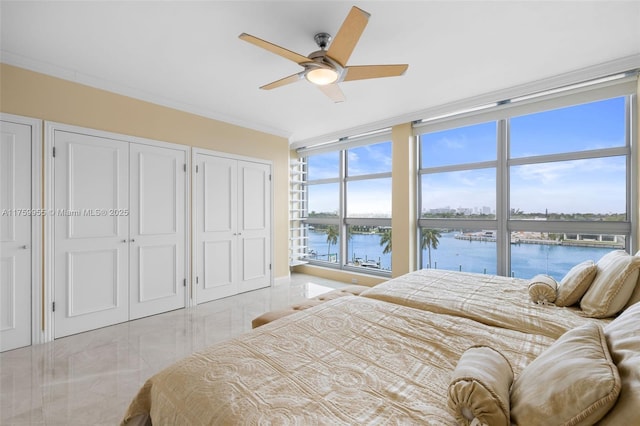 bedroom with multiple closets, a water view, marble finish floor, ornamental molding, and a ceiling fan