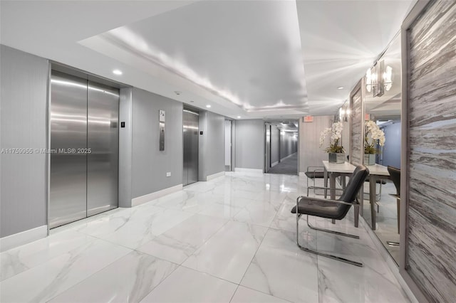 hallway featuring a raised ceiling, elevator, recessed lighting, and marble finish floor