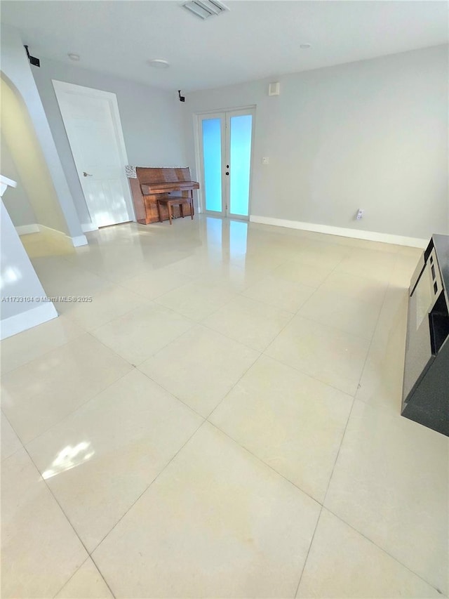 unfurnished room with visible vents, french doors, arched walkways, light tile patterned flooring, and baseboards