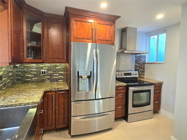 kitchen featuring stone countertops, stainless steel appliances, glass insert cabinets, wall chimney exhaust hood, and backsplash