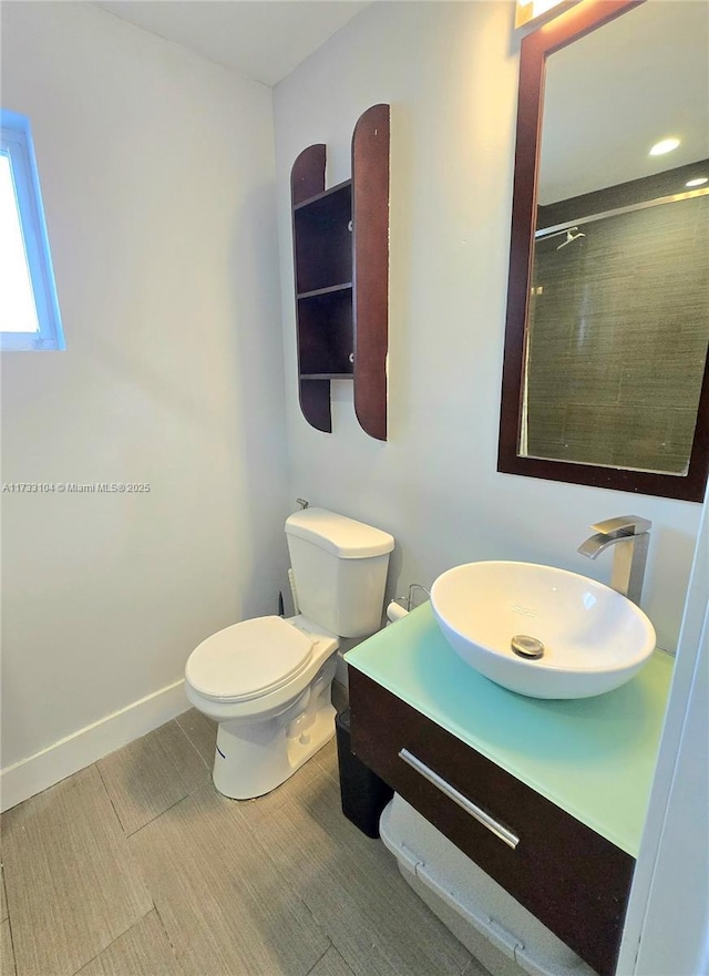 bathroom featuring vanity, wood finished floors, baseboards, a tile shower, and toilet