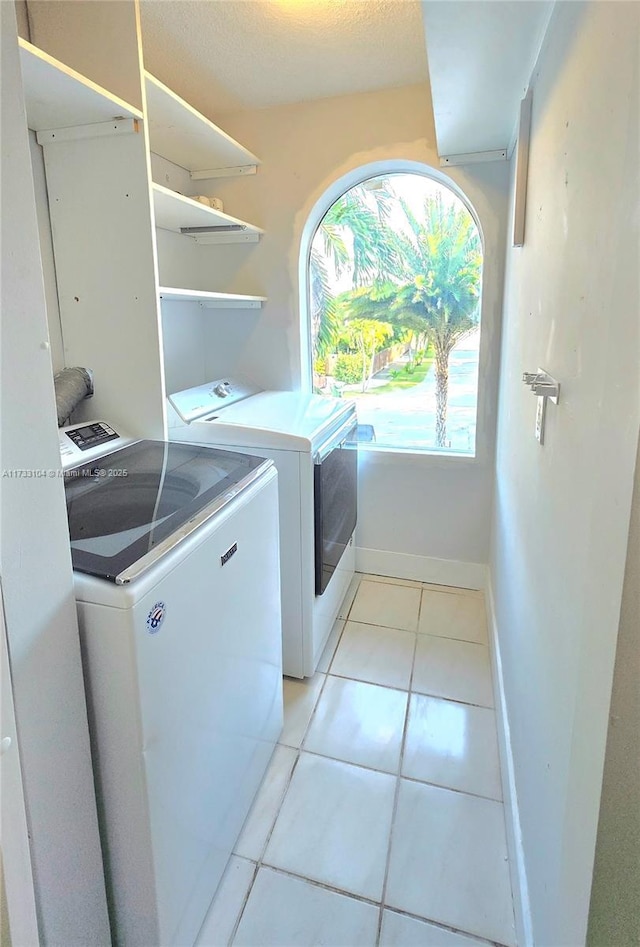 clothes washing area with baseboards, light tile patterned flooring, washing machine and dryer, and laundry area