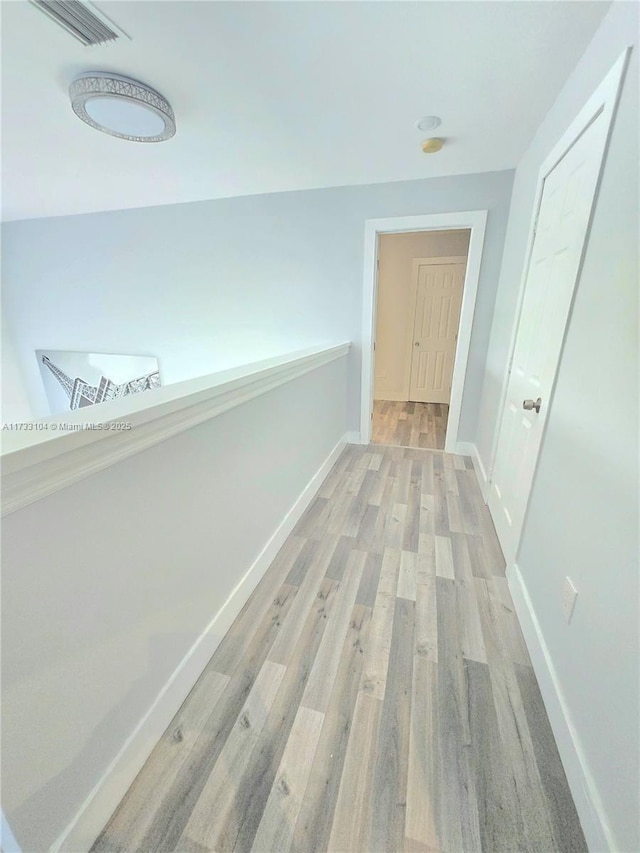 hallway with light wood-type flooring, visible vents, and baseboards