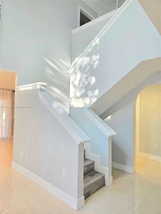 stairway featuring tile patterned floors, a high ceiling, baseboards, and arched walkways