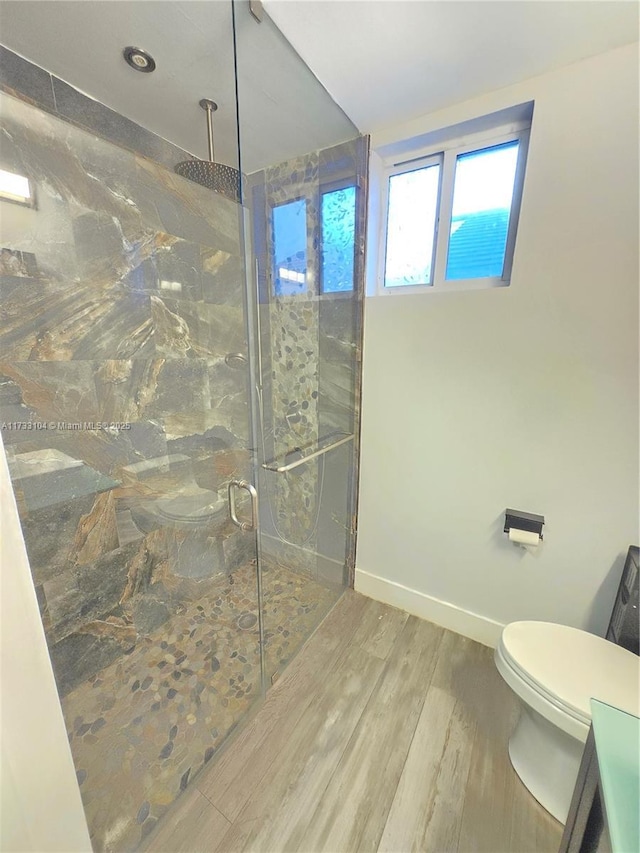 bathroom featuring toilet, wood finished floors, baseboards, and a marble finish shower