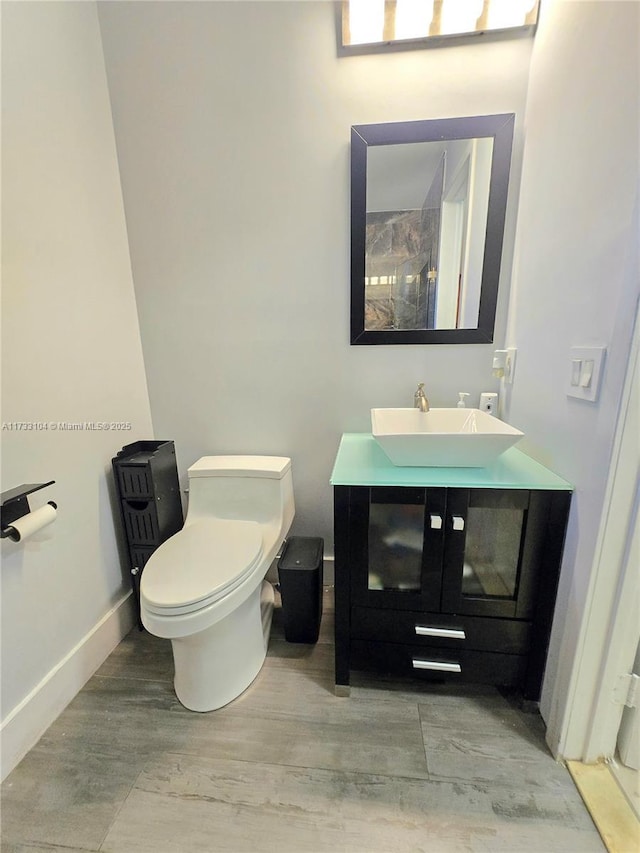 bathroom with vanity, wood finished floors, baseboards, walk in shower, and toilet