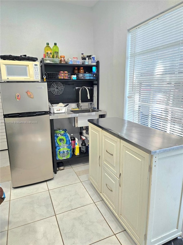 kitchen featuring white microwave, dark countertops, light tile patterned floors, freestanding refrigerator, and a sink