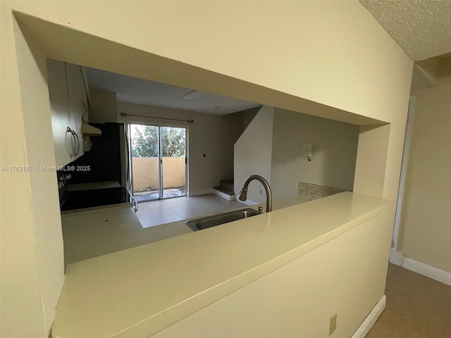 kitchen with baseboards, a peninsula, a sink, light countertops, and under cabinet range hood