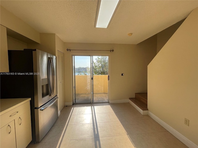 kitchen featuring light tile patterned floors, a textured ceiling, baseboards, and stainless steel fridge with ice dispenser