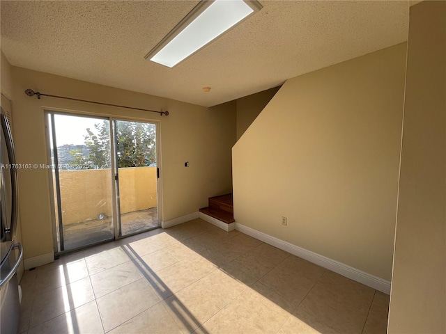 unfurnished room featuring baseboards, a textured ceiling, light tile patterned flooring, and stairs