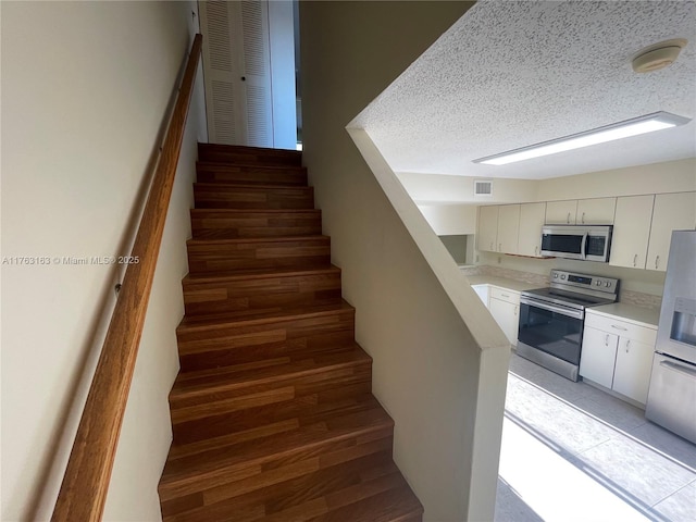 stairs with tile patterned flooring, visible vents, and a textured ceiling