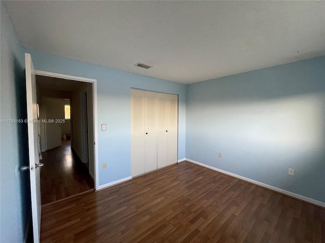 unfurnished bedroom with a closet, baseboards, visible vents, and dark wood-style flooring