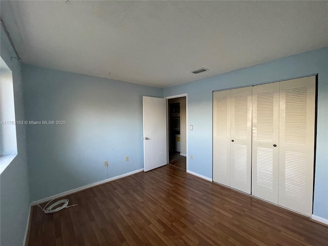 unfurnished bedroom featuring a closet, visible vents, baseboards, and wood finished floors