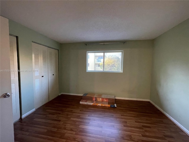 unfurnished bedroom featuring baseboards, a textured ceiling, wood finished floors, and multiple closets