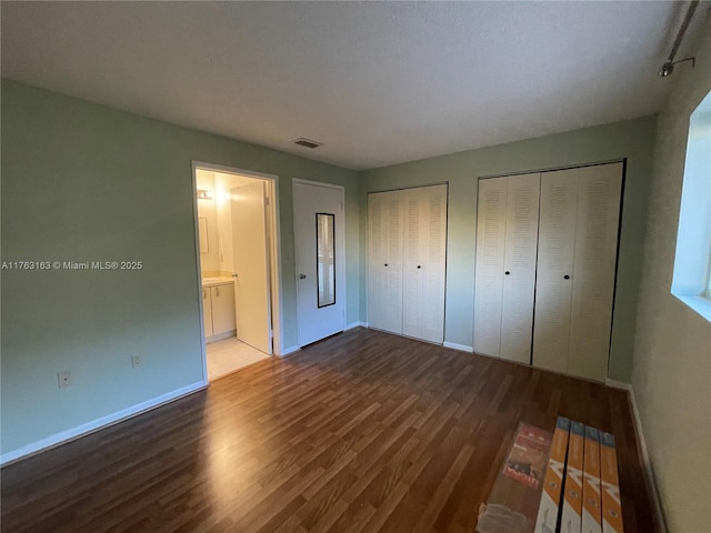 unfurnished bedroom with visible vents, baseboards, two closets, and wood finished floors