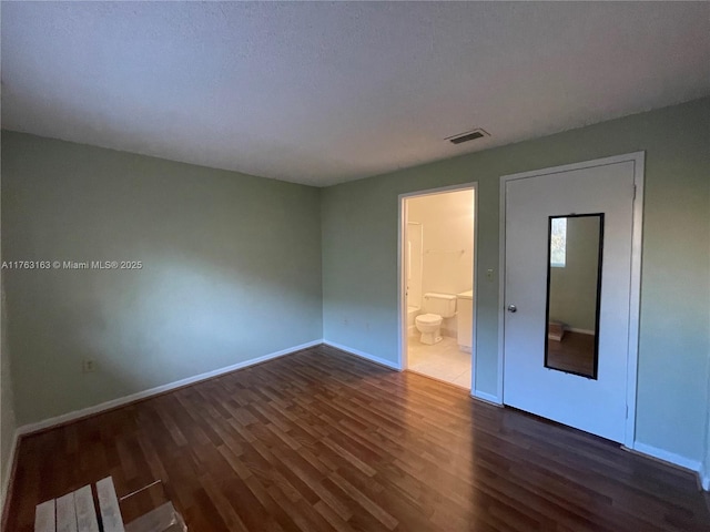 spare room featuring visible vents, baseboards, and dark wood-style flooring