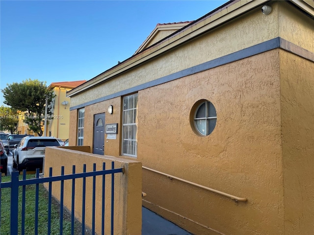 view of side of home with stucco siding and fence