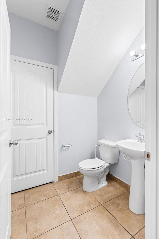 half bathroom featuring baseboards, visible vents, lofted ceiling, tile patterned flooring, and toilet