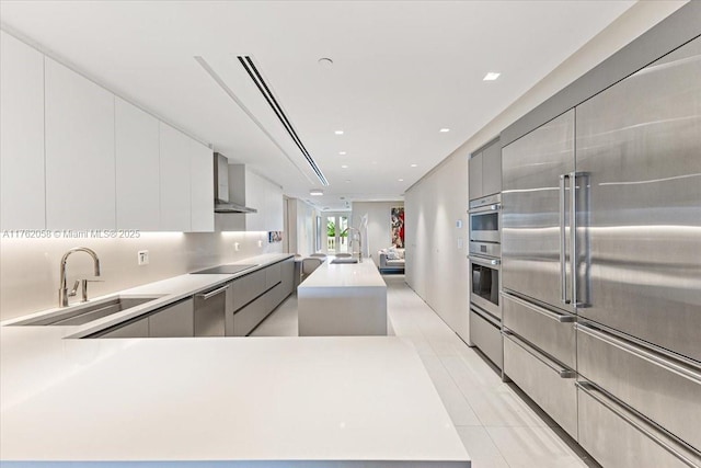 kitchen with stainless steel appliances, a sink, light countertops, wall chimney exhaust hood, and modern cabinets