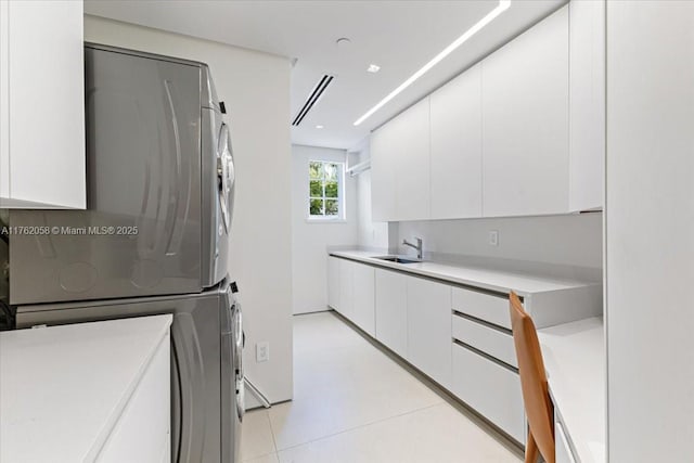 laundry room with a sink, light tile patterned floors, cabinet space, and stacked washing maching and dryer