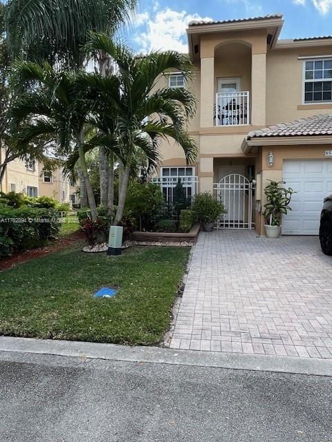 view of front of home featuring a front yard, stucco siding, decorative driveway, a balcony, and a gate