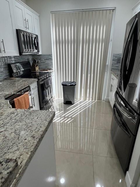 kitchen with tasteful backsplash, light stone countertops, light tile patterned floors, white cabinets, and black appliances