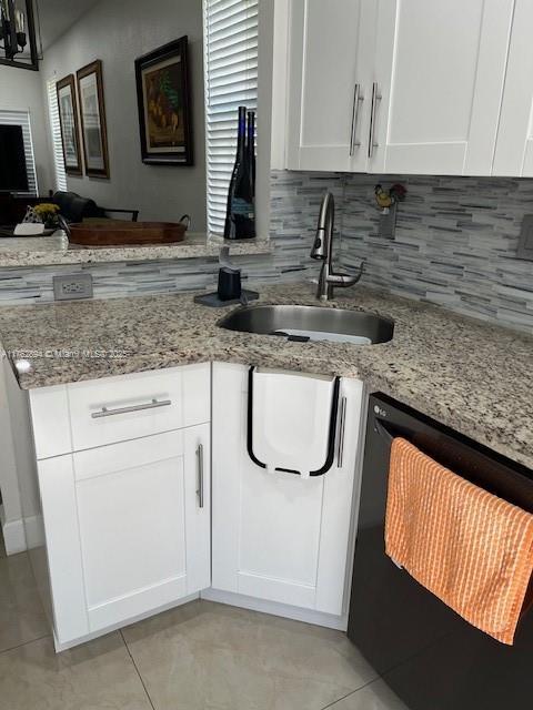 kitchen featuring light stone counters, a peninsula, a sink, black dishwasher, and tasteful backsplash