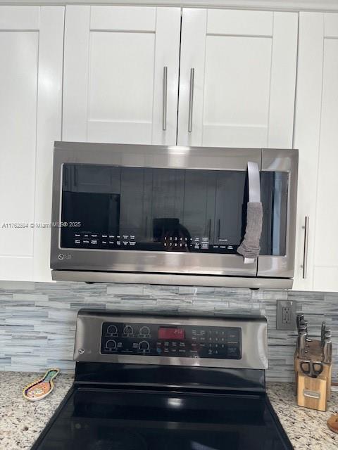 interior details with white cabinetry, light stone counters, tasteful backsplash, and stainless steel appliances