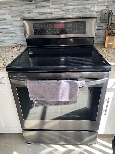 room details with stainless steel electric stove, light stone countertops, and tasteful backsplash