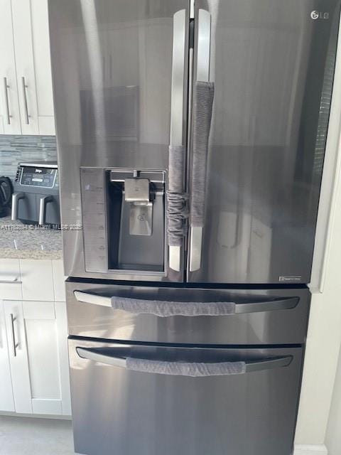 room details with white cabinets, light stone counters, stainless steel refrigerator with ice dispenser, and backsplash