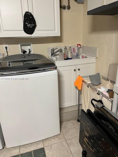 clothes washing area featuring a sink, cabinet space, washer / dryer, and light tile patterned floors