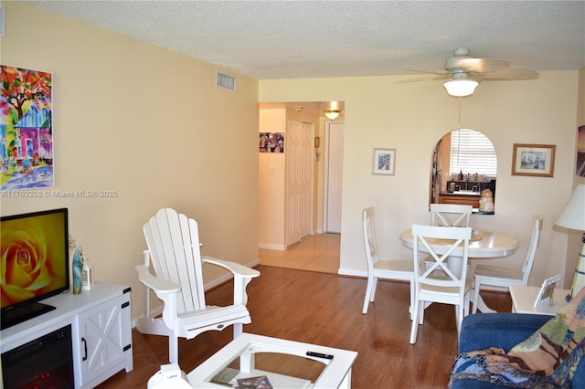 living area featuring visible vents, a textured ceiling, wood finished floors, baseboards, and ceiling fan