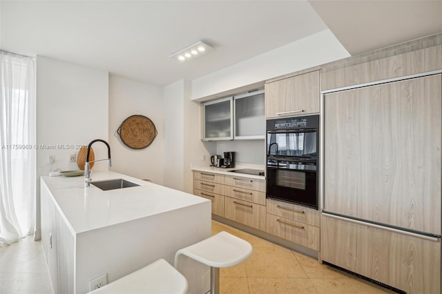 kitchen with black appliances, light brown cabinets, a sink, light countertops, and glass insert cabinets