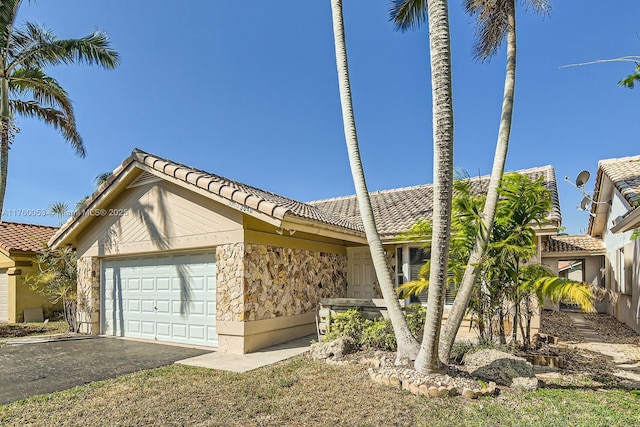 view of front of house with a tiled roof, an attached garage, stone siding, and driveway