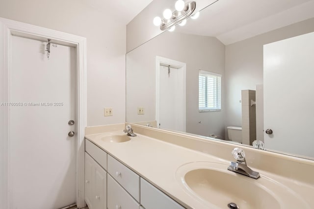 bathroom with lofted ceiling, toilet, double vanity, and a sink