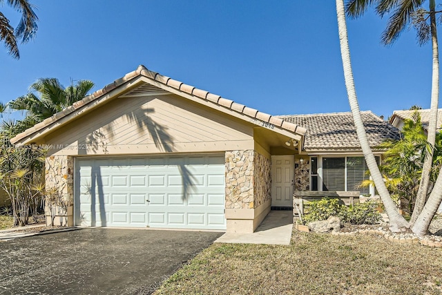 view of front of home featuring stone siding, an attached garage, a tile roof, and driveway