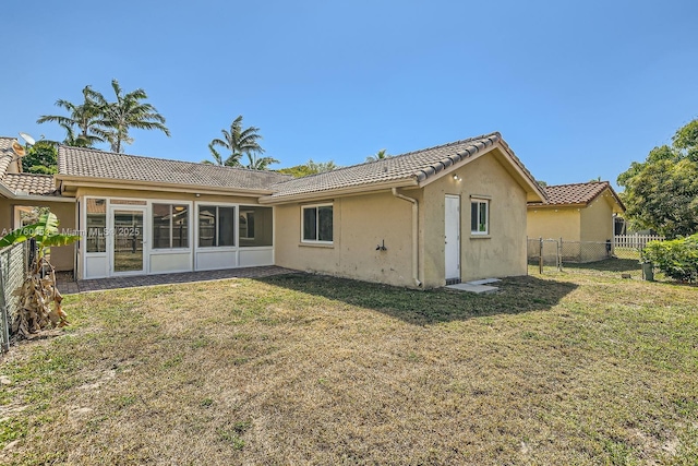 back of property featuring stucco siding, a tiled roof, a lawn, and fence