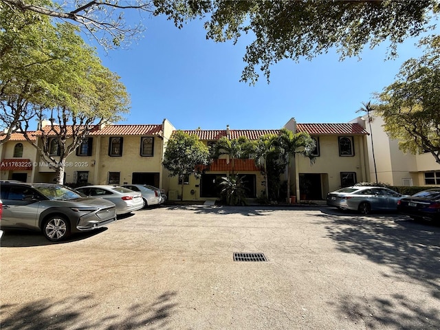 townhome / multi-family property featuring a tiled roof, uncovered parking, and stucco siding