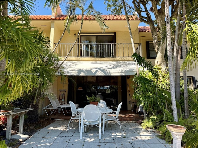 back of property with a tile roof, stucco siding, a balcony, a patio area, and outdoor dining space