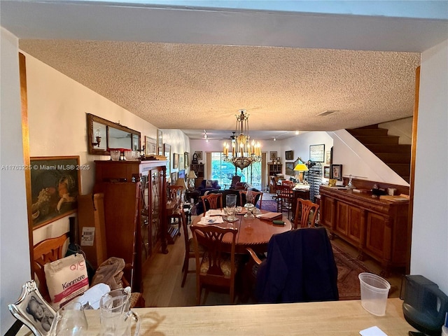 dining room with an inviting chandelier, stairway, wood finished floors, and a textured ceiling