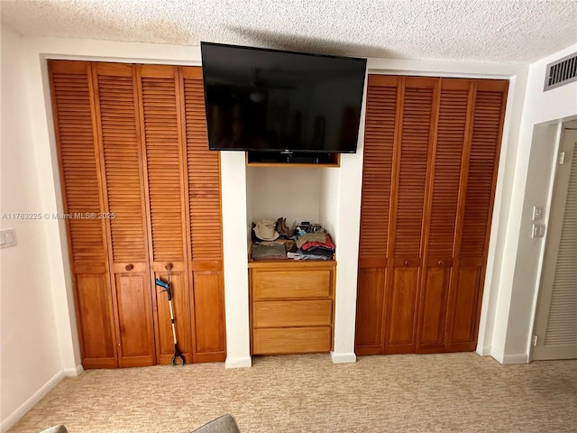 bedroom featuring light carpet, a textured ceiling, and two closets