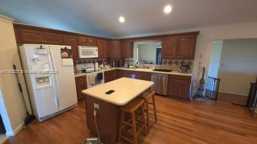 kitchen featuring a center island, light countertops, decorative backsplash, wood finished floors, and white appliances