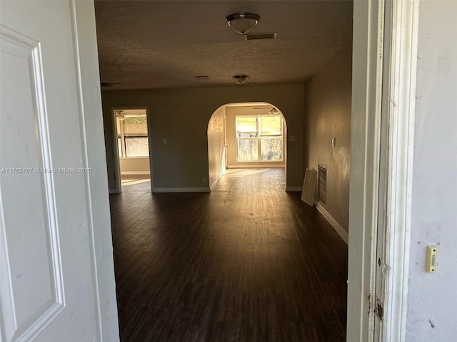 corridor featuring arched walkways, visible vents, a textured ceiling, and dark wood-type flooring