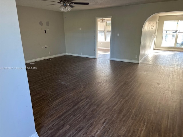 unfurnished room featuring a ceiling fan, a textured ceiling, dark wood finished floors, arched walkways, and baseboards