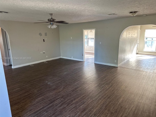 empty room featuring visible vents, a ceiling fan, arched walkways, baseboards, and dark wood-style flooring