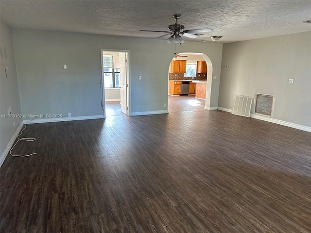 unfurnished room featuring a ceiling fan, visible vents, baseboards, dark wood finished floors, and arched walkways